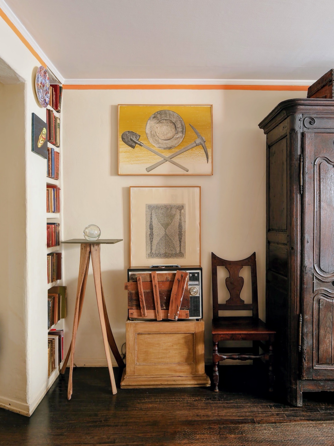 Interior with framed artworks, books, an antique chair, and a dark wooden cabinet