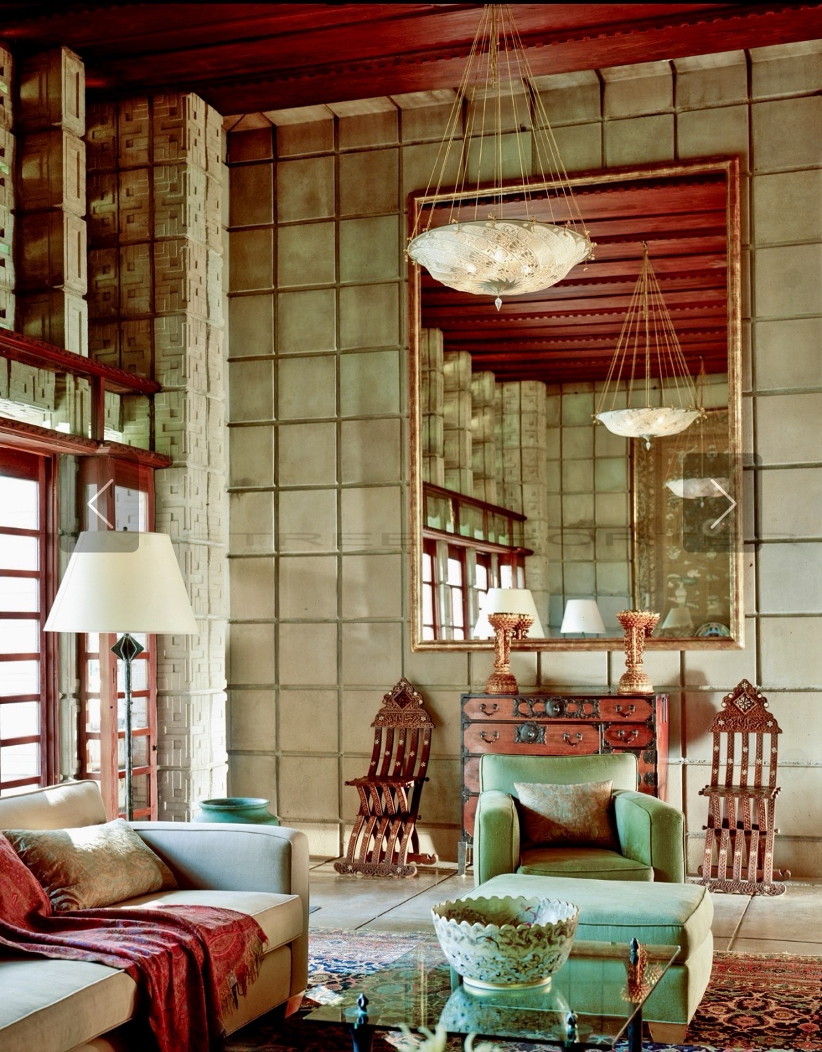 Living room at Frank Lloyd Wright’s La Miniatura, decorated by Annie Kelly, with patterned concrete walls, a large mirror, and green seating